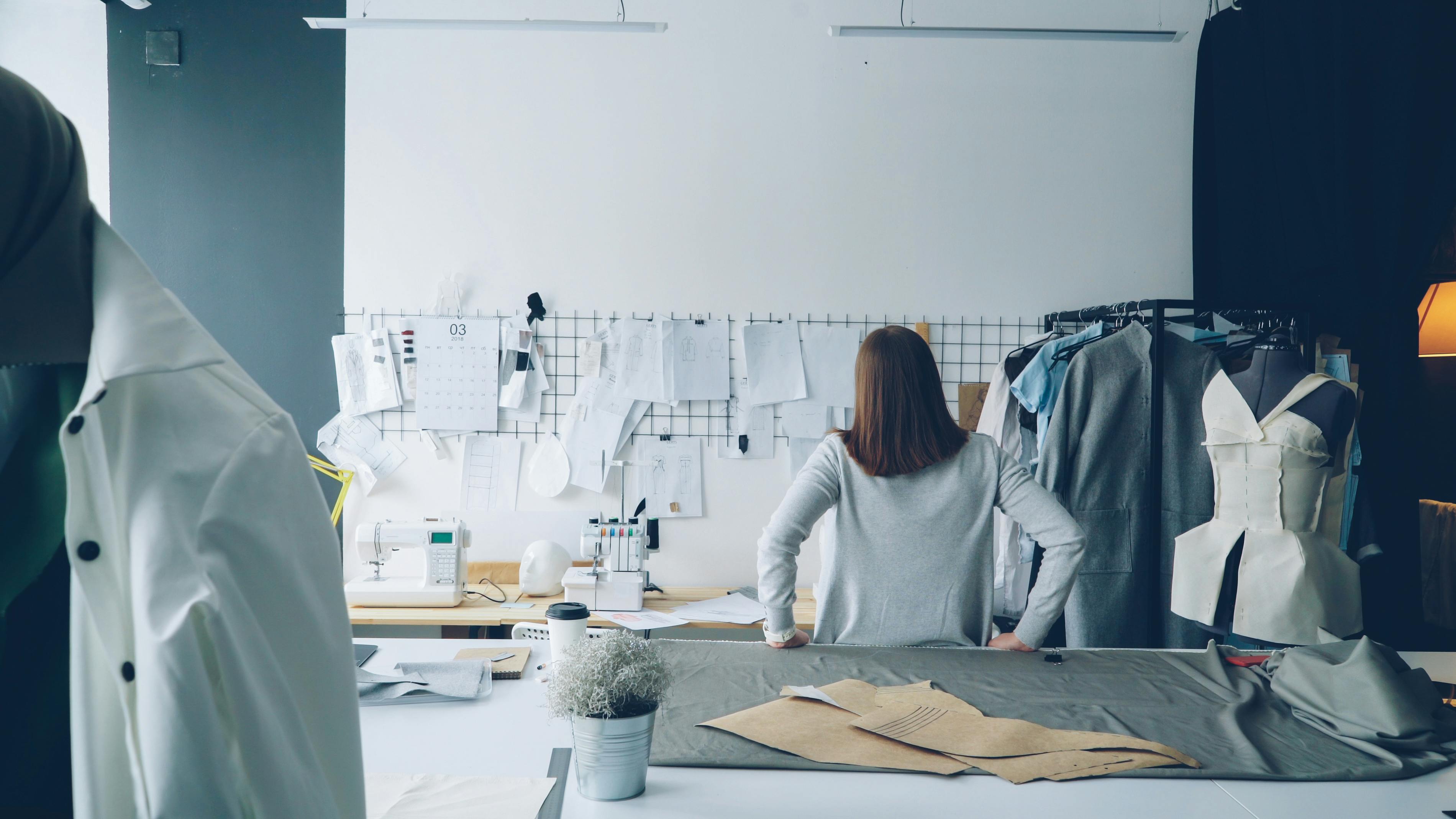 Fashion designer in studio surrounded by sewing patterns and garments.