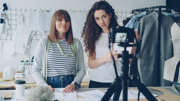 Two female fashion designers discuss their work in a trendy studio with sewing patterns.