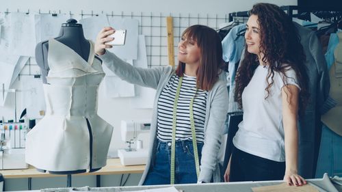 Free Two young fashion designers take a selfie with a handmade dress in a studio setting. Stock Photo
