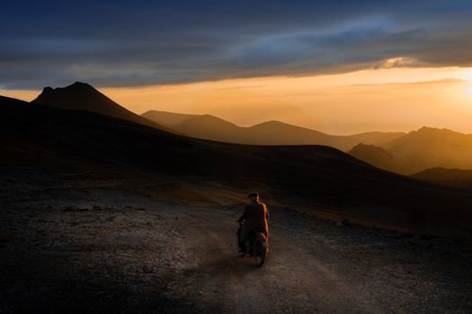 A lone motorcyclist rides along a rugged mountain path during a stunning sunset on Erciyes Mountain.