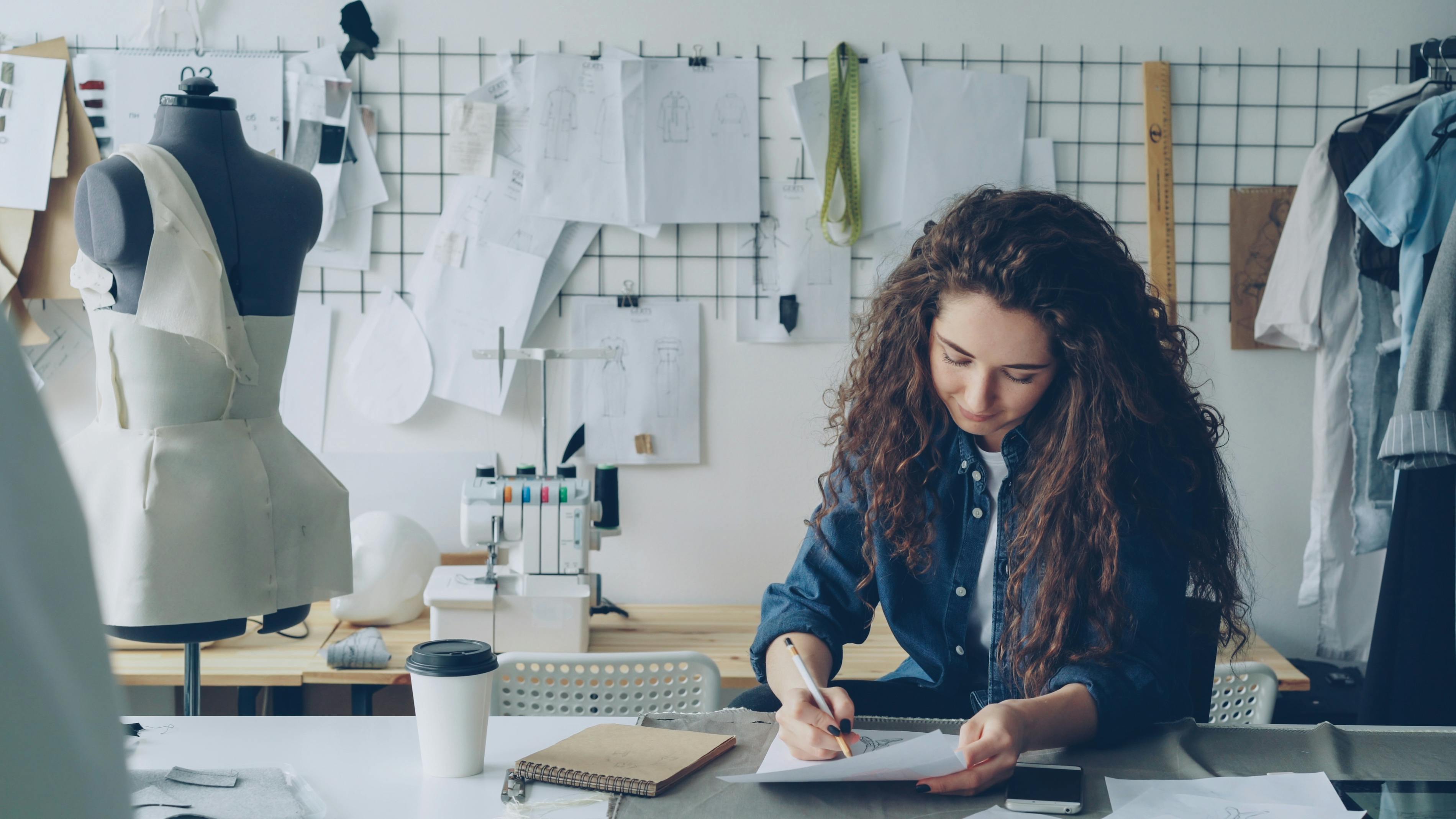 A female fashion designer sketches in her studio with a sewing mannequin.