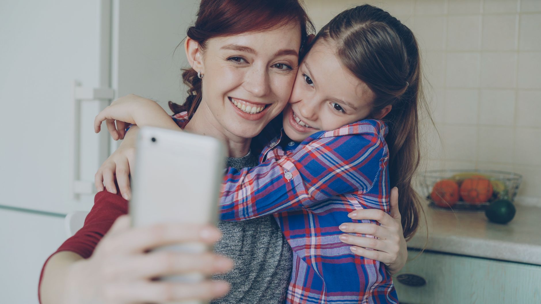 Smiling mother and daughter taking a selfie in a cozy indoor setting.