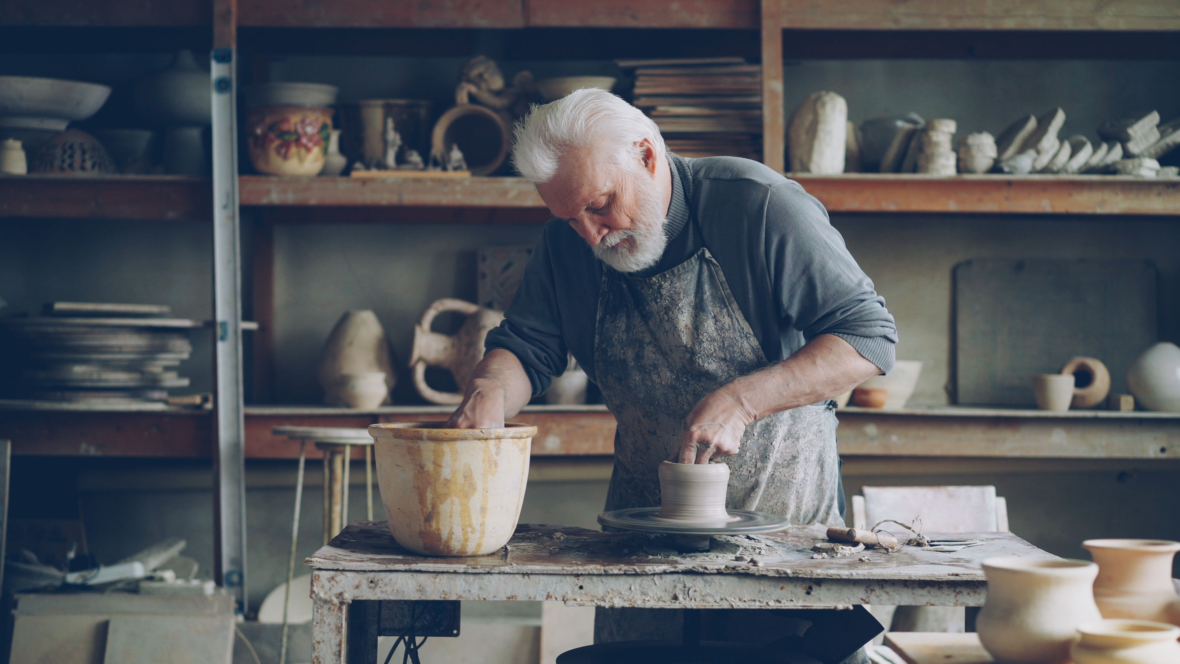 Senior male potter focused on shaping clay pottery in a traditional studio environment.