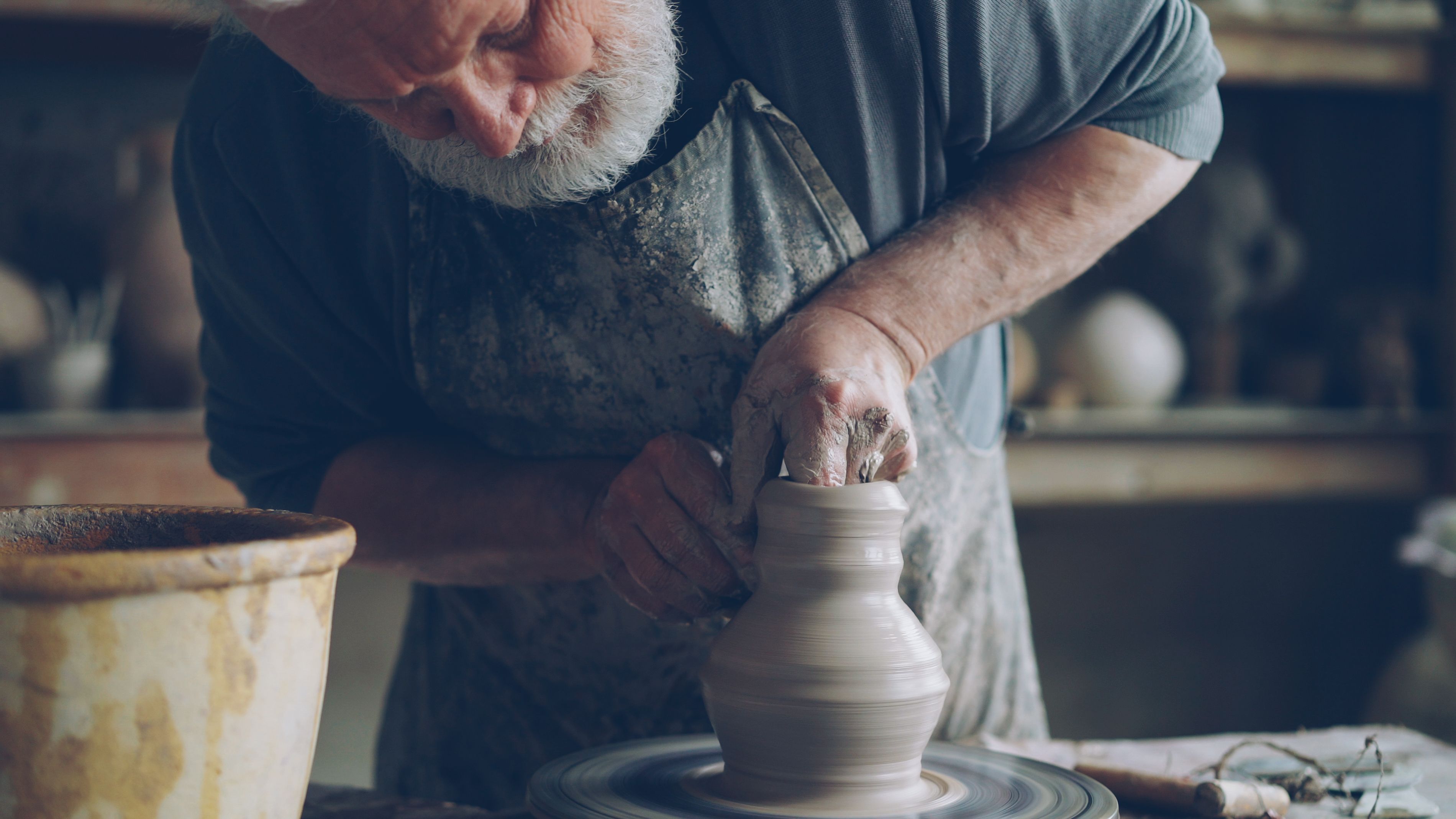 Senior male potter shaping clay on pottery wheel in rustic studio setting.