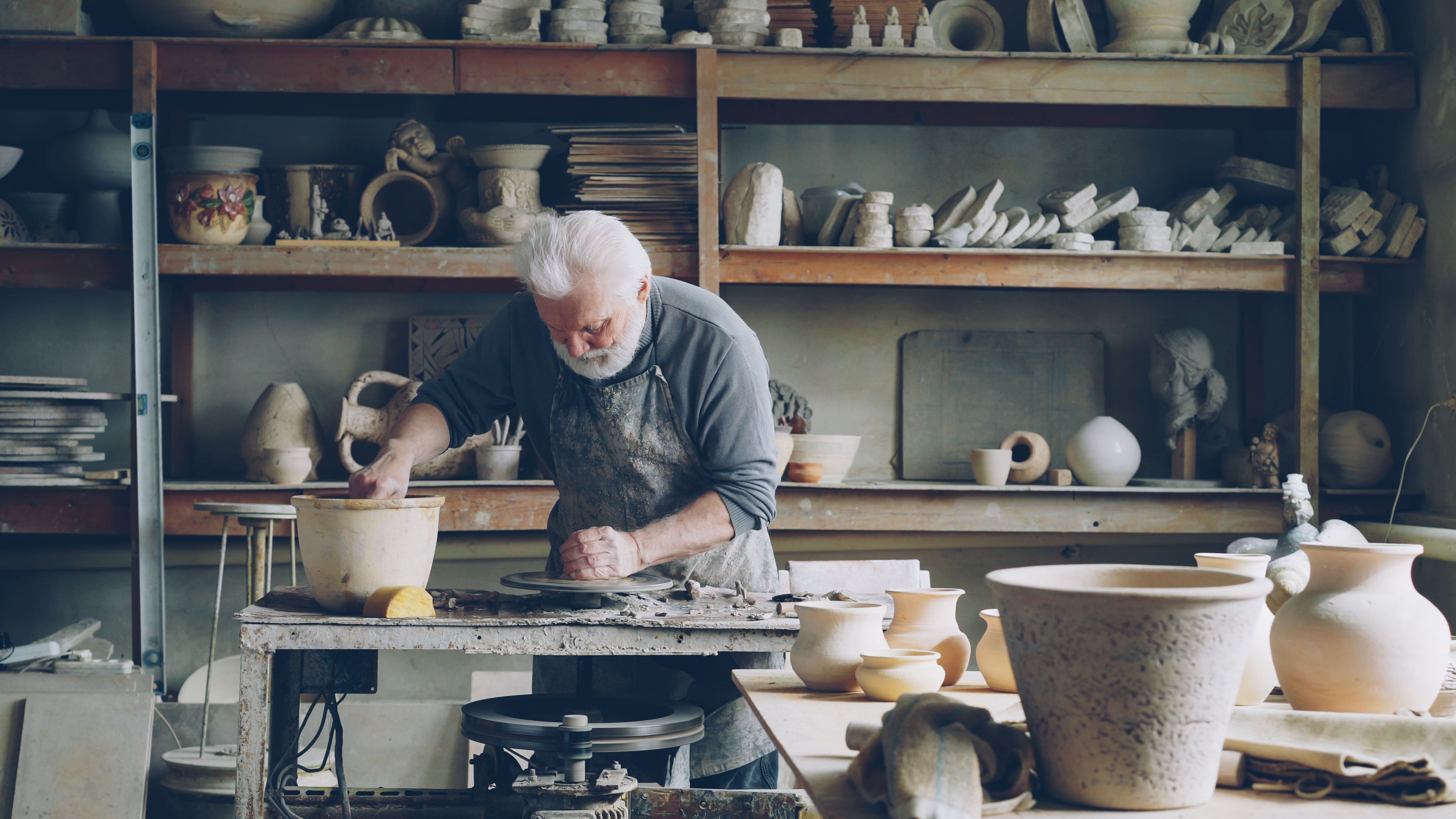 Elderly potter works diligently in a rustic studio, crafting handmade pottery.