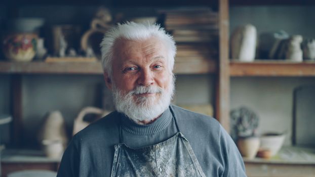 Portrait of a senior male potter smiling in his workshop.