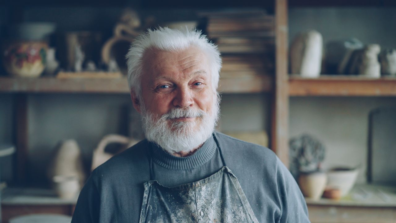 portrait of a senior male potter smiling in his workshop