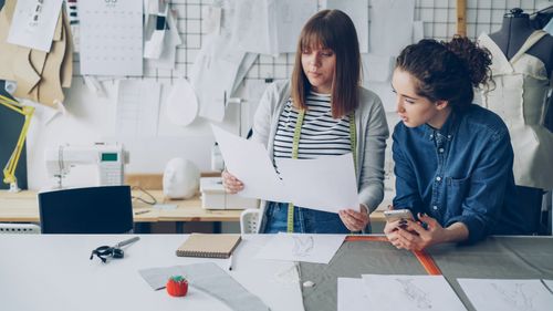 Free Two fashion designers discussing clothing sketches in a design studio. Stock Photo