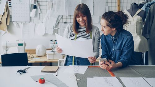 Free Two fashion designers review sketches in a creative studio environment. Stock Photo