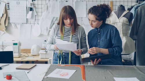 Free Two female fashion designers reviewing patterns and plans in a studio setting. Stock Photo