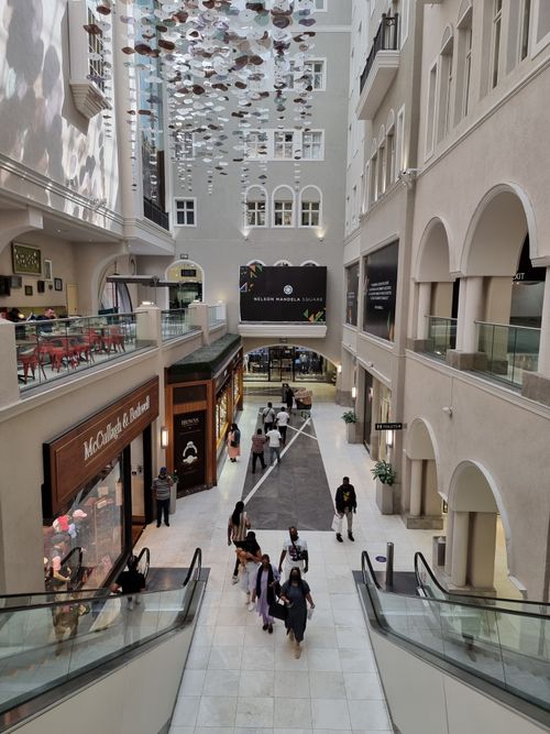 Free View of Nelson Mandela Square, Sandton. A modern shopping center with people, stores, and escalators. Stock Photo
