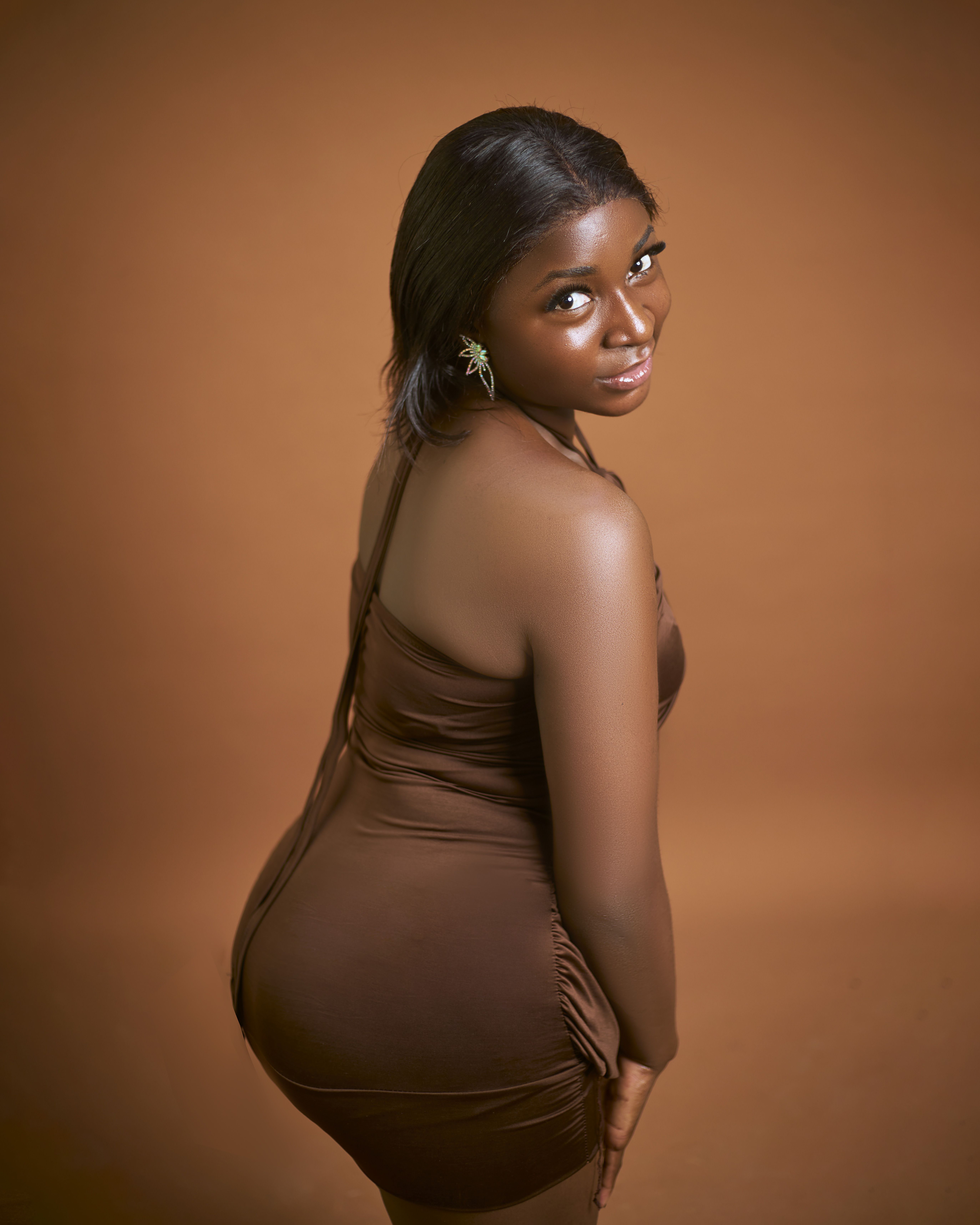 Posed Photo of a Young Black Woman in a Brown Dress Sitting on a Chair  Against a Pink Background  Free Stock Photo
