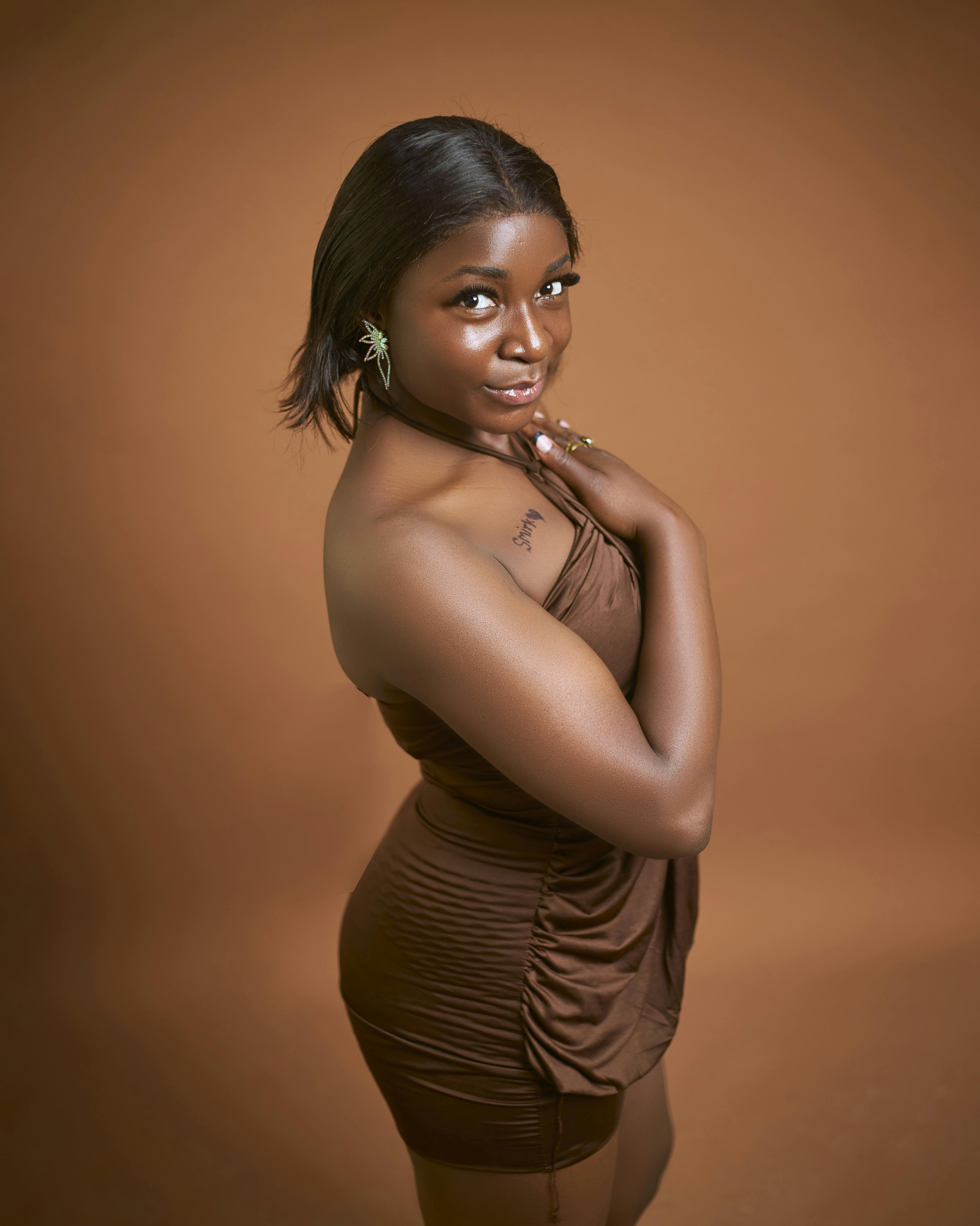Chic portrait of a woman in a stylish brown dress against a warm backdrop.