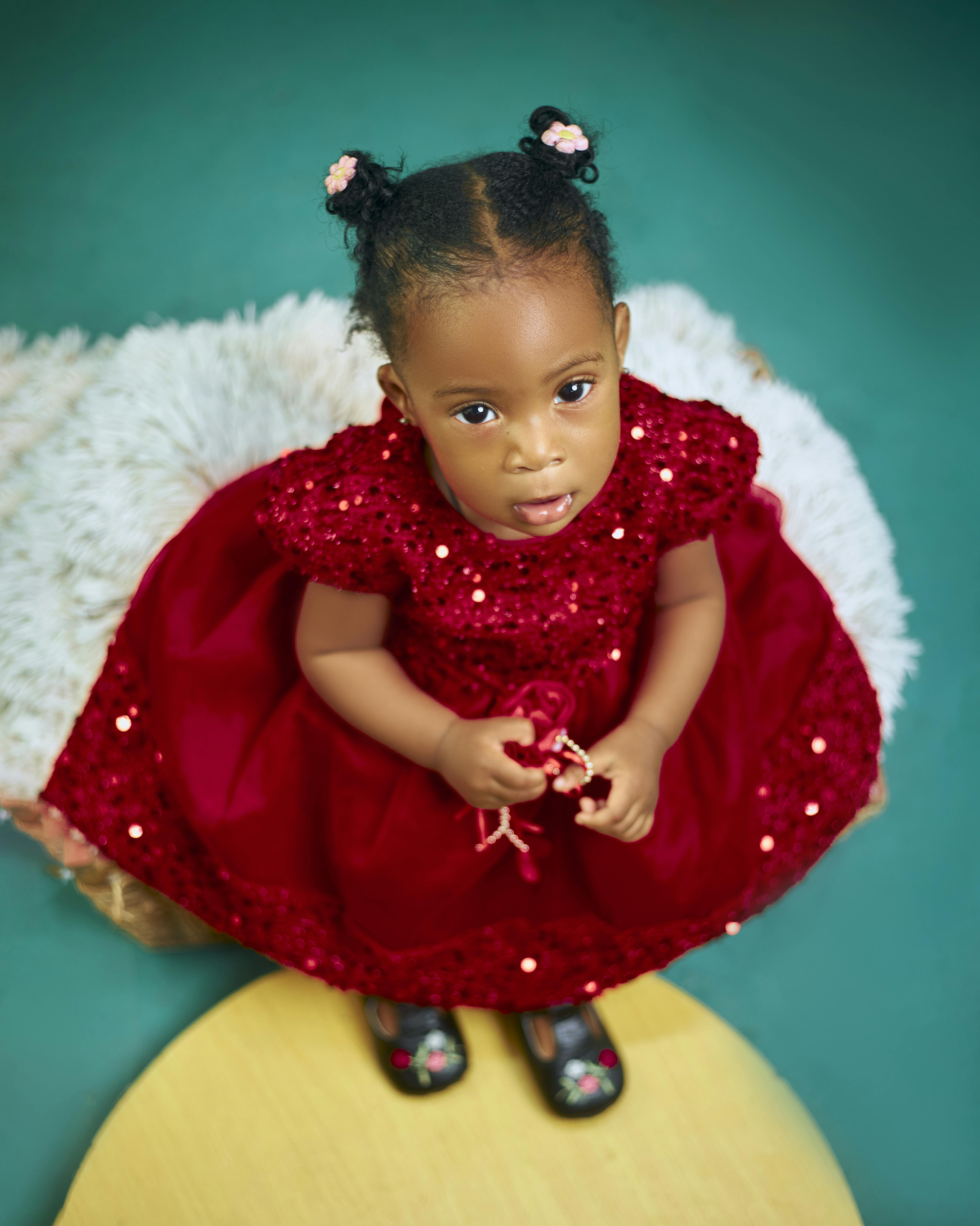 Cute toddler in a red sequin dress looking up with a sweet expression.