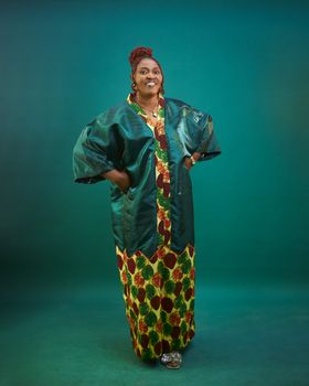 Elegant portrait of an adult woman in colorful traditional African attire on a solid teal background.