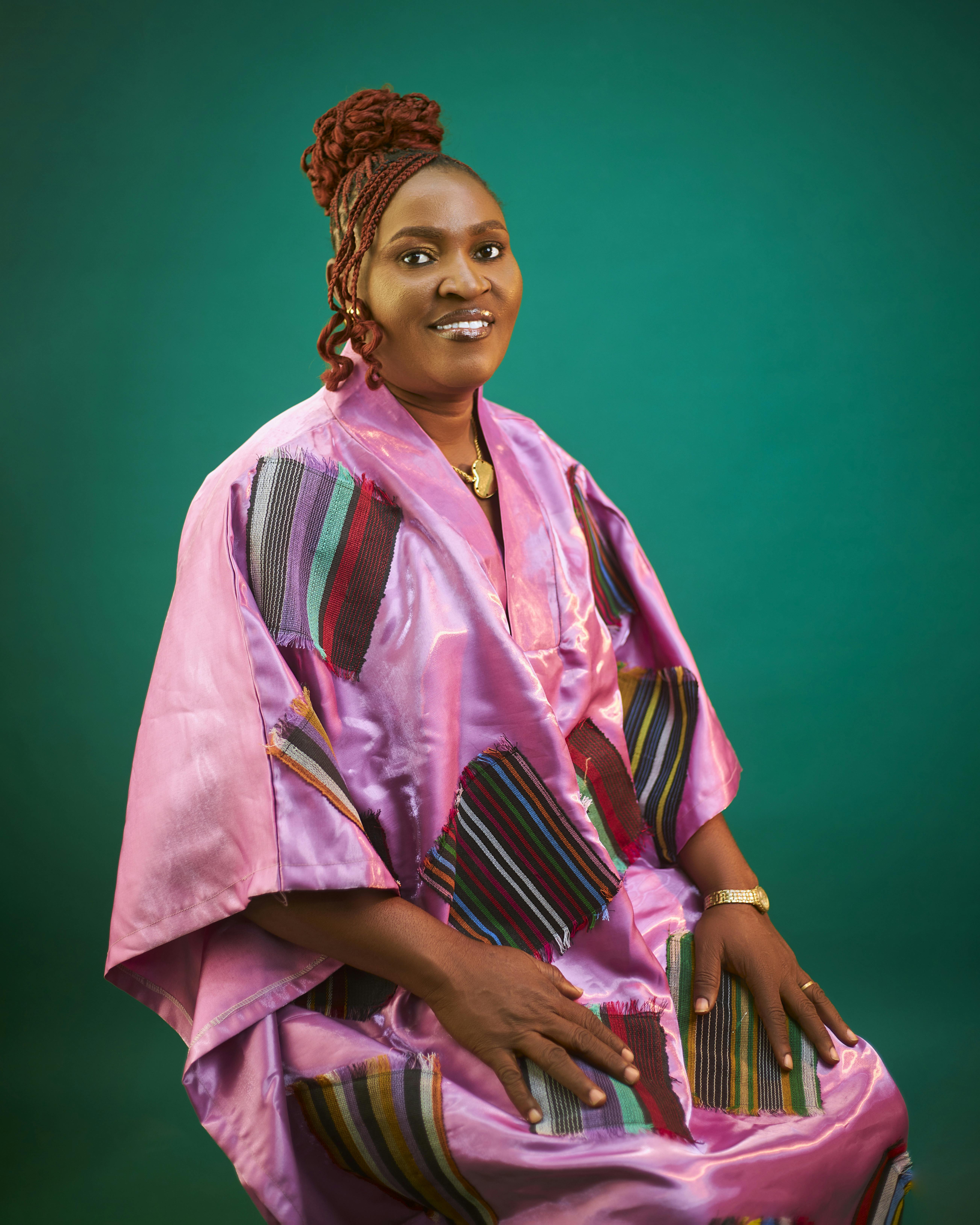 Portrait of a smiling woman in bright traditional dress with green backdrop.