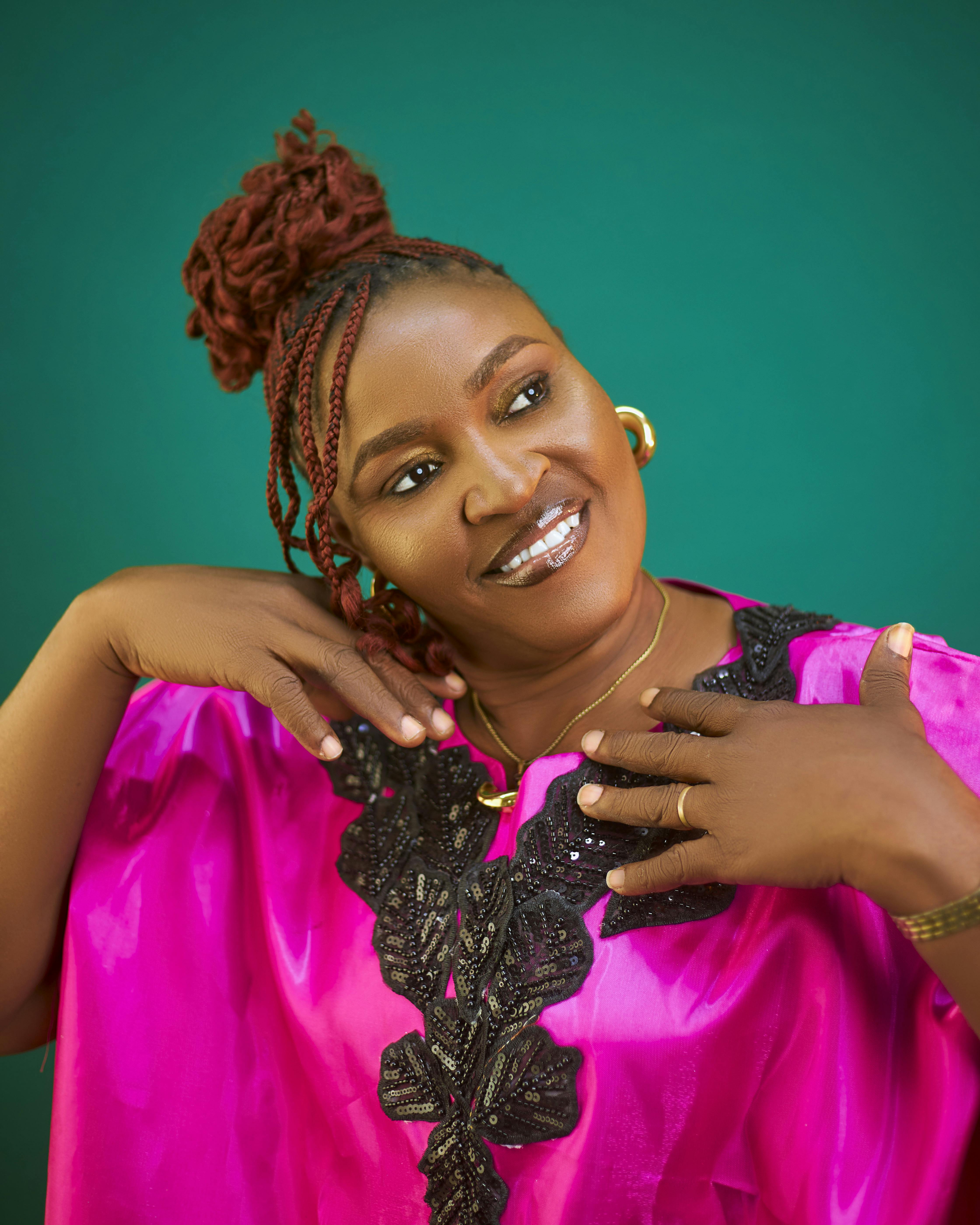 Portrait of a smiling African woman in vibrant traditional attire on a green background.