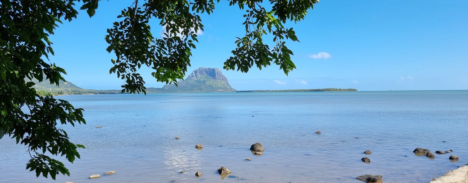 A tranquil coastal scene of Le Morne Brabant, Mauritius with clear blue water and lush green foliage.