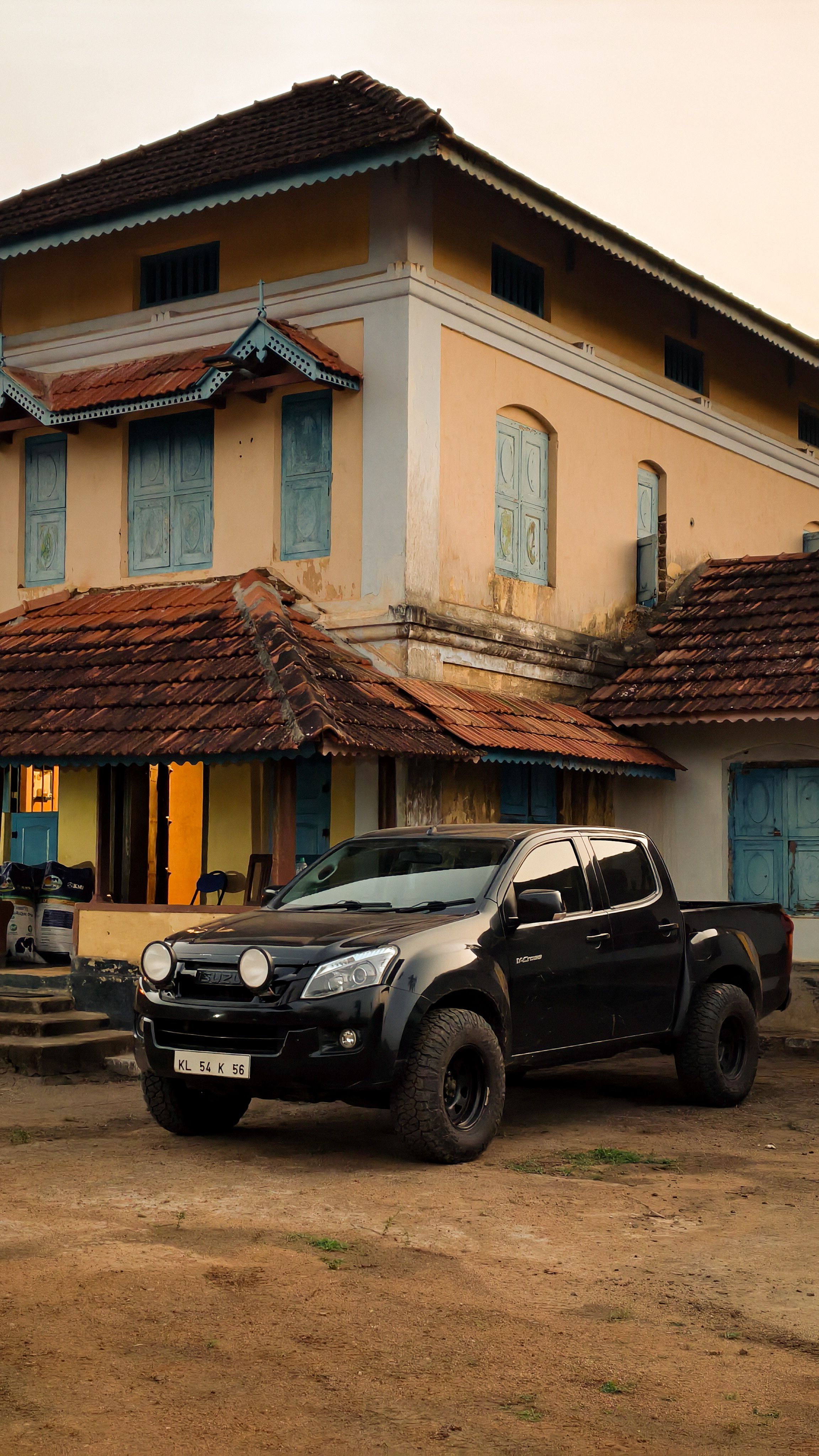 Rustic Kerala house with a stylish black pickup foregrounded, creating a stark contrast.