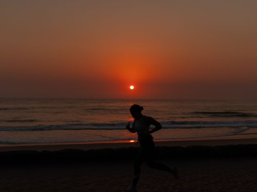 Free A person jogging on a beach with a stunning sunset in the background. Stock Photo