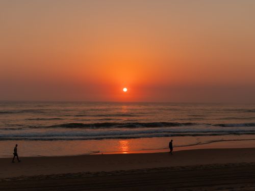 Free Serene beach sunset with two people walking along the shore, reflecting tranquility. Stock Photo