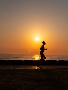 A silhouette of a person running along the ocean shore during a picturesque sunset.