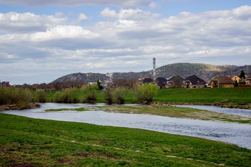 Free Idyllic landscape with a river, village, and hills under a partly cloudy sky. Stock Photo