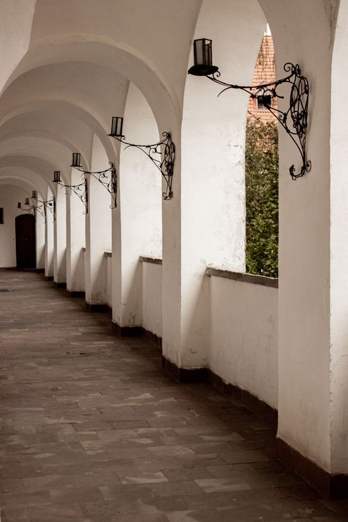 Free A serene view of a historic arched hallway with ornate wall lanterns. Stock Photo