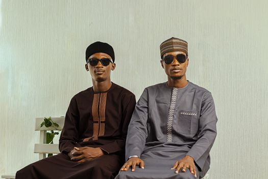 Two men in sunglasses wearing traditional Nigerian attire indoors.