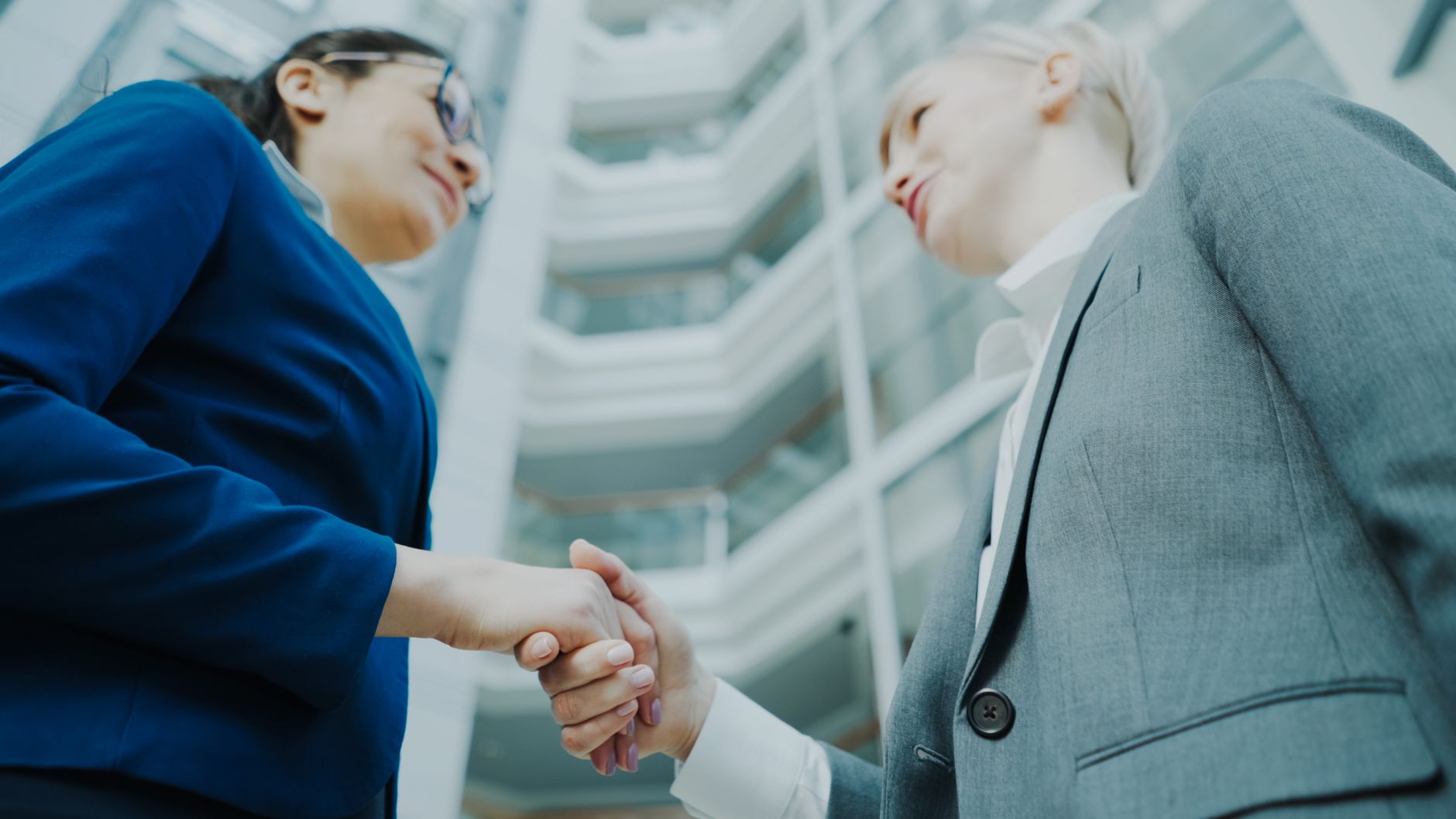 點亮設計品牌顧問 - 網頁設計 logo設計 平面設計 Two business professionals shaking hands in a modern office atrium, symbolizing collaboration.