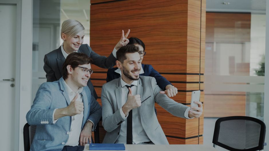 Colegas de oficina en trajes tomando una selfie divertida con el pulgar hacia arriba.