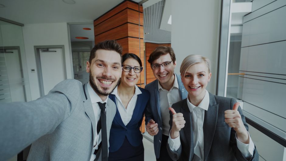 Un equipo de negocios alegre tomándose un selfie en un ambiente de oficina moderno.