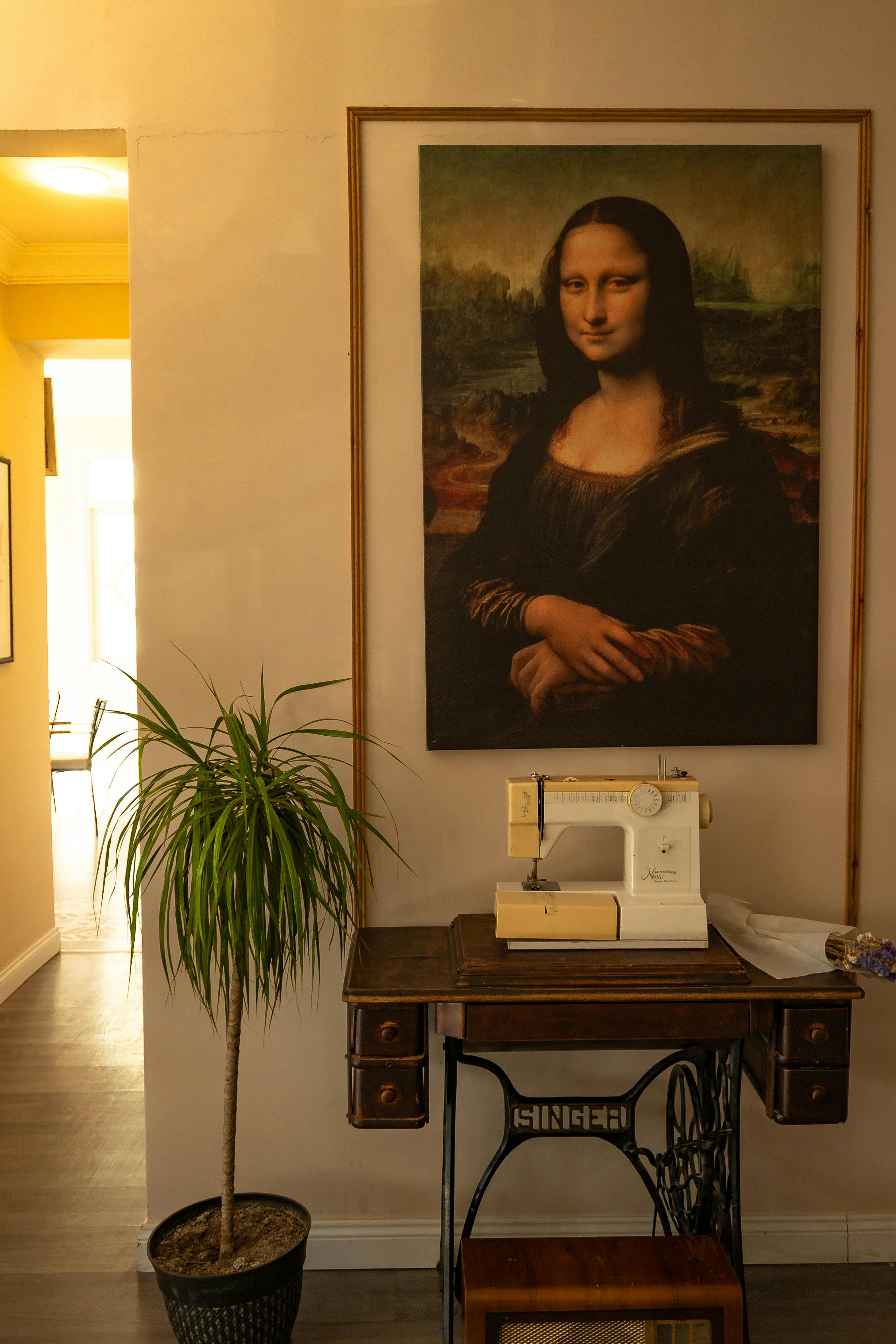 A vintage sewing machine under a Mona Lisa poster next to a potted plant.