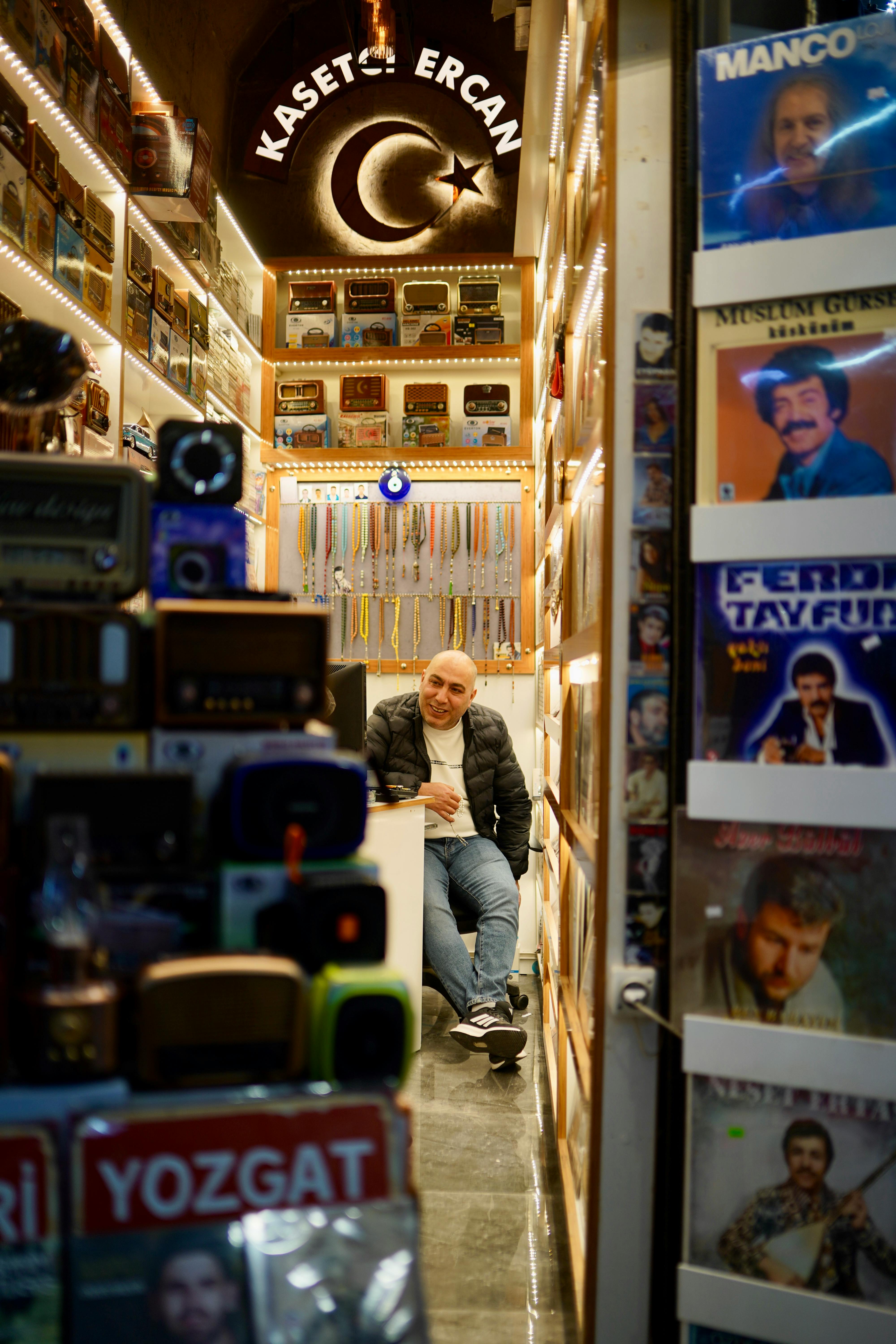 Cozy vintage store with retro electronics and vinyl records, featuring a man sitting amidst nostalgic decor.