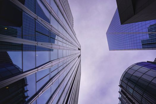 A dramatic upward view of glass skyscrapers against a cloudy sky, showcasing modern architecture.