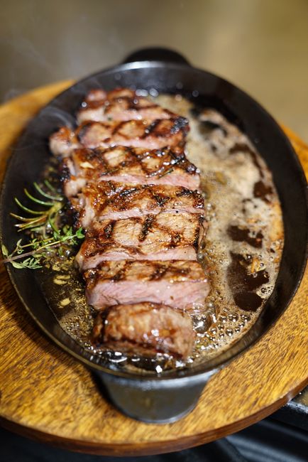 A thick ribeye steak with a dark brown crust resting in a cast iron skillet, basted with melted butter, garlic cloves, and sprigs of thyme.