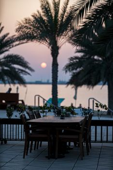Peaceful outdoor dining setup by the lake at sunset with palm trees in view.