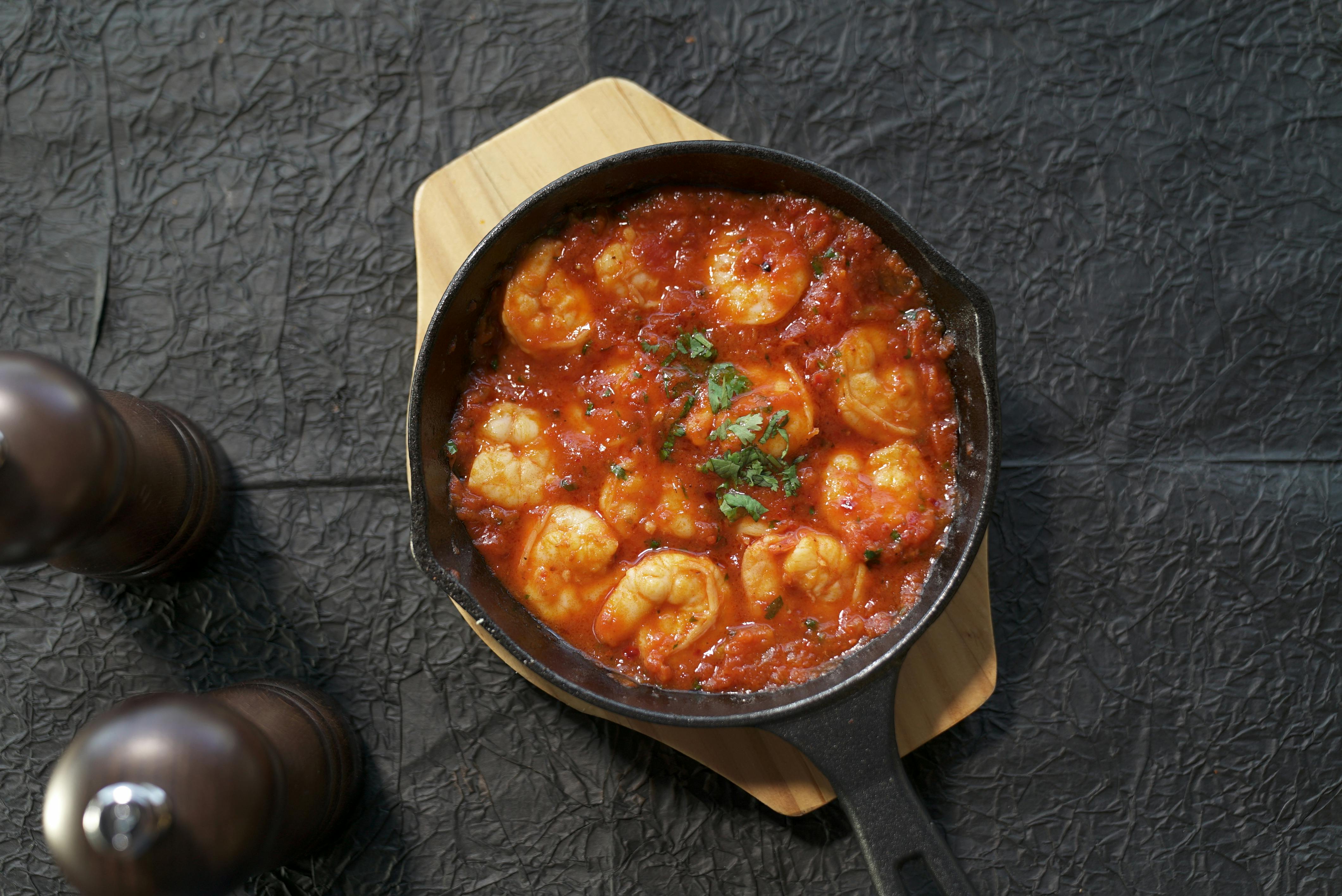 Tasty shrimp cooked in tomato sauce served in a cast iron skillet, garnished with fresh herbs, creating a warm and inviting meal.