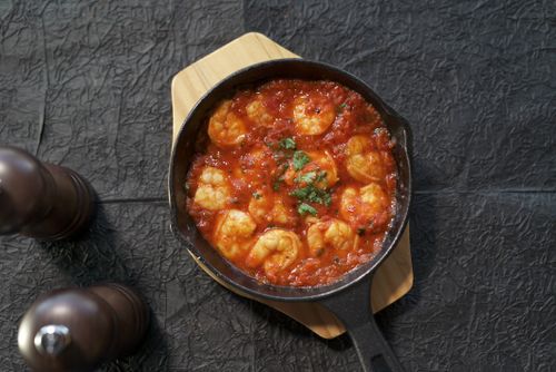 Free Tasty shrimp cooked in tomato sauce served in a cast iron skillet, garnished with fresh herbs, creating a warm and inviting meal. Stock Photo