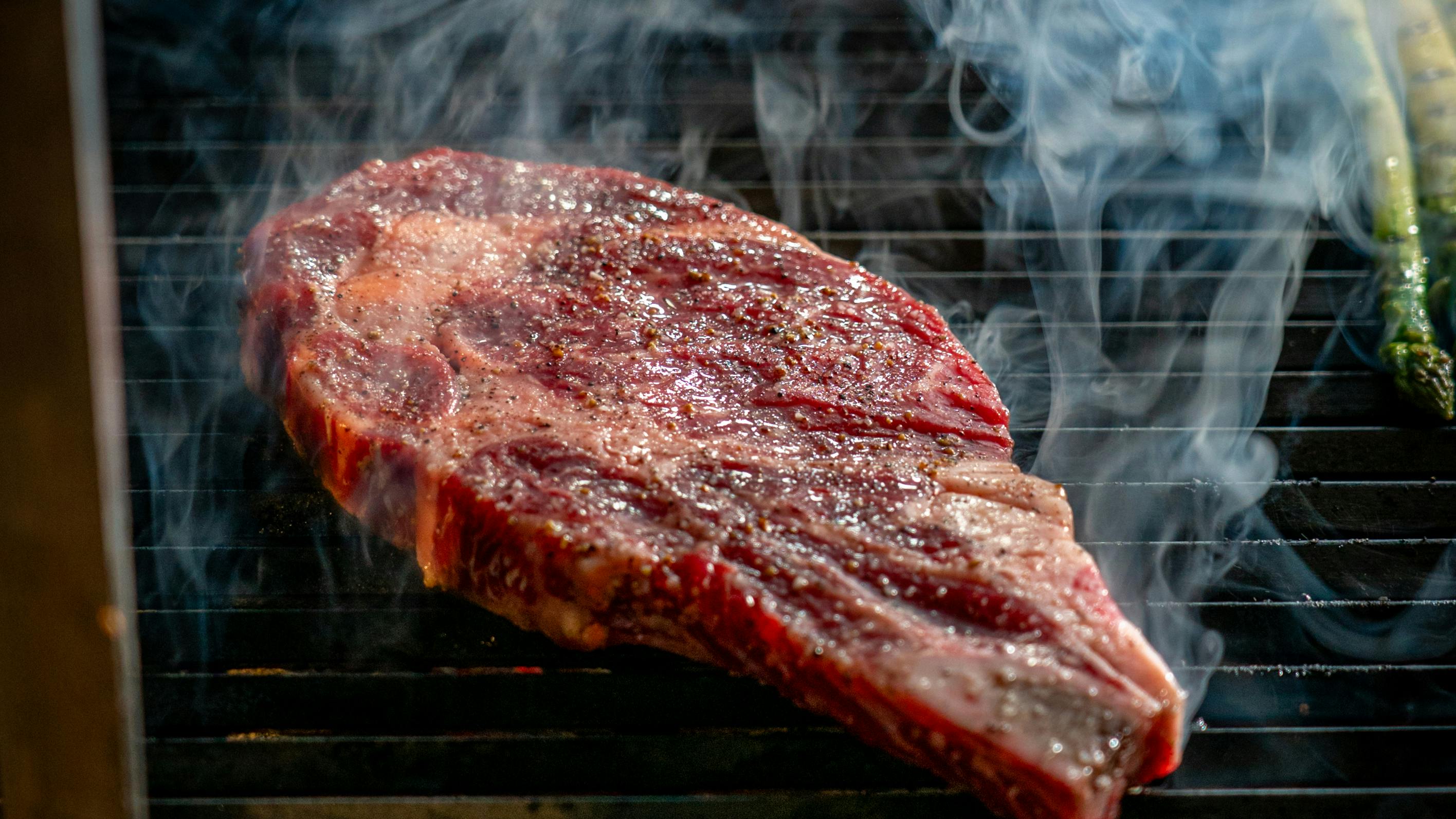 Close-up of a juicy steak sizzling on the grill with visible smoke, perfect for barbecue enthusiasts.