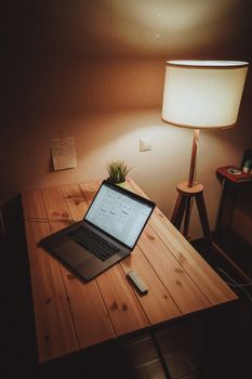 A warm and inviting workspace featuring a laptop on a wooden desk, illuminated by a standing lamp.