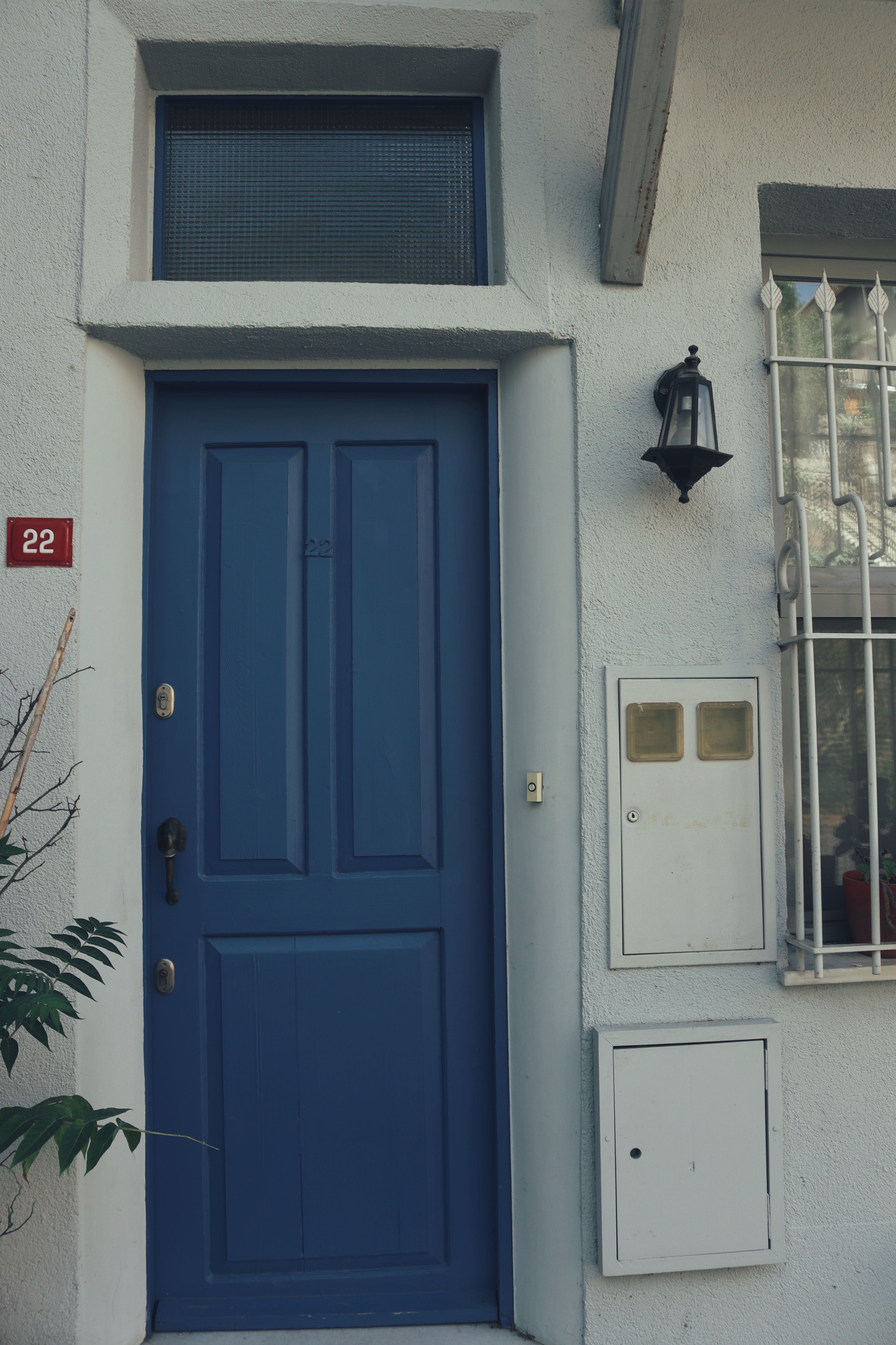 Aesthetic blue door on a white building facade, adorned with a classic lamp and number 22.