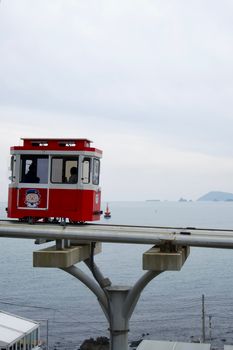 A red monorail in motion along the coastline, offering a scenic view of the ocean and distant islands. — photo by Gasper Selakovic