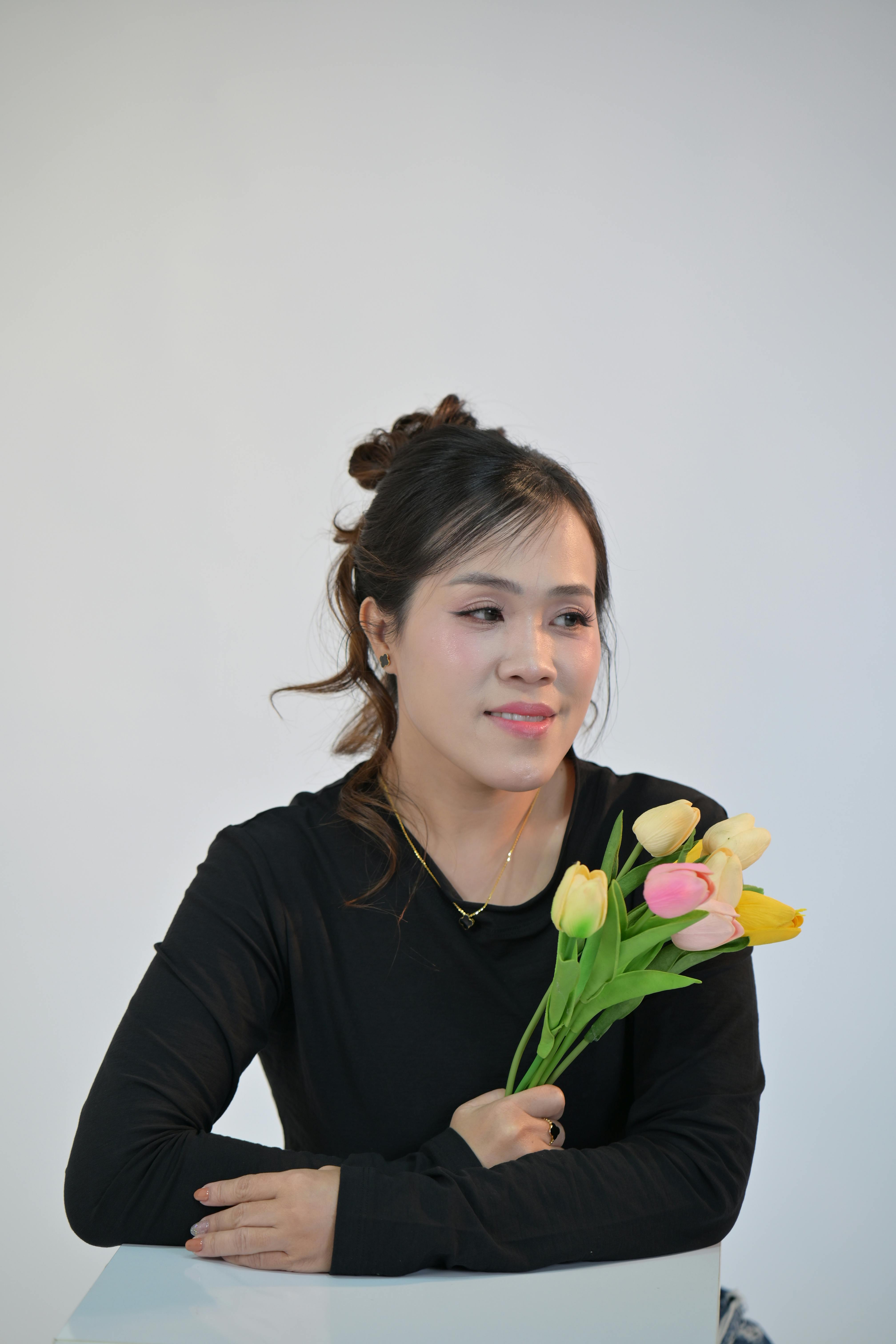 A serene portrait of a woman in black sweater holding colorful tulips against a minimalistic background.