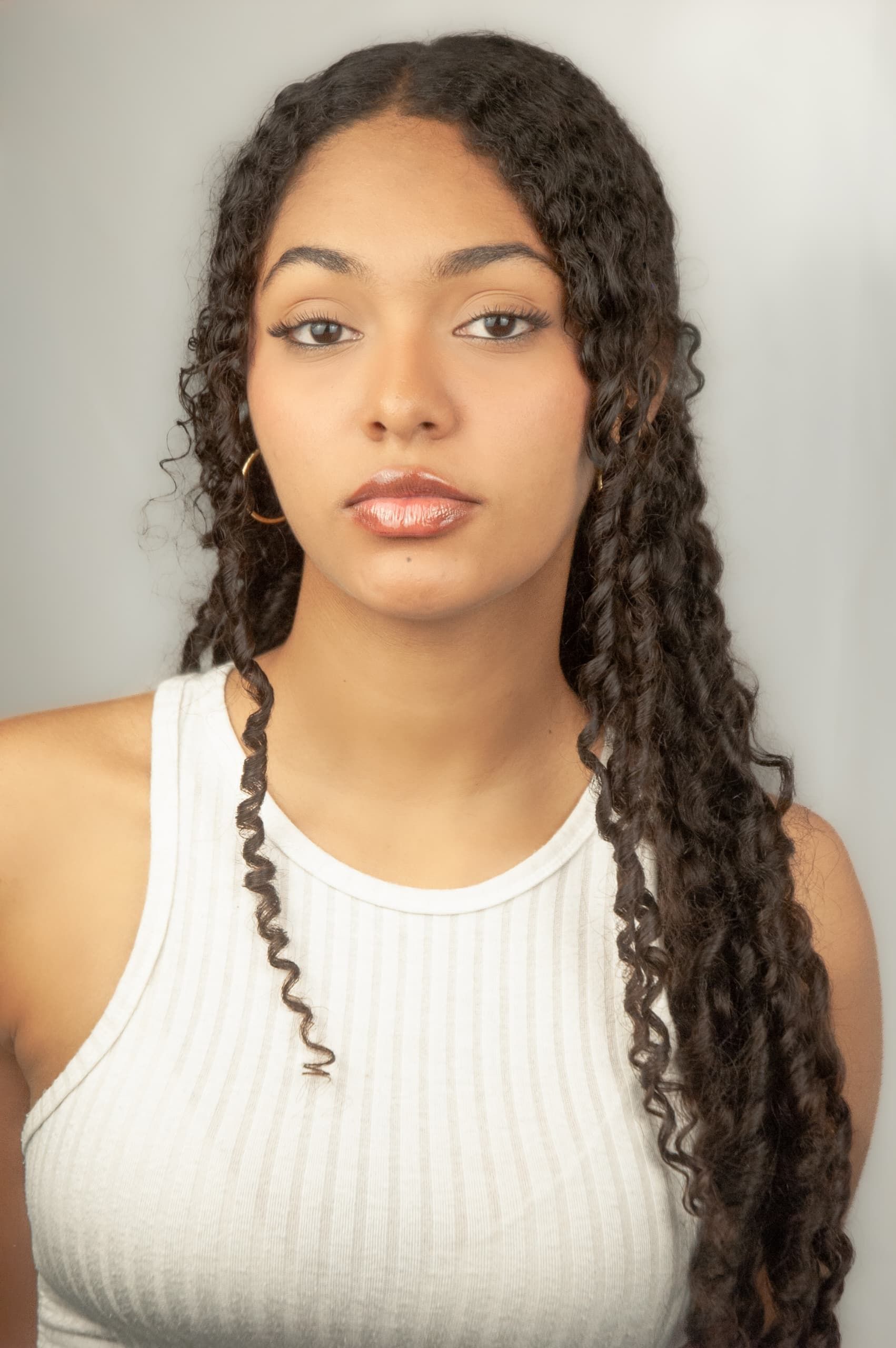 Elegant young woman with curly hair in white top on neutral background.