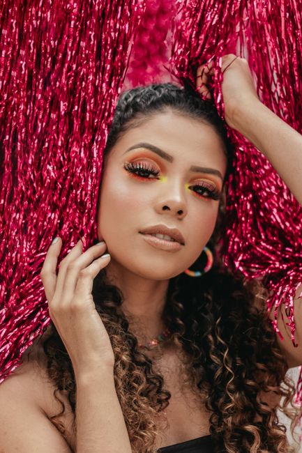 A young woman striking a pose with vibrant eye makeup, surrounded by bright pink tinsel.