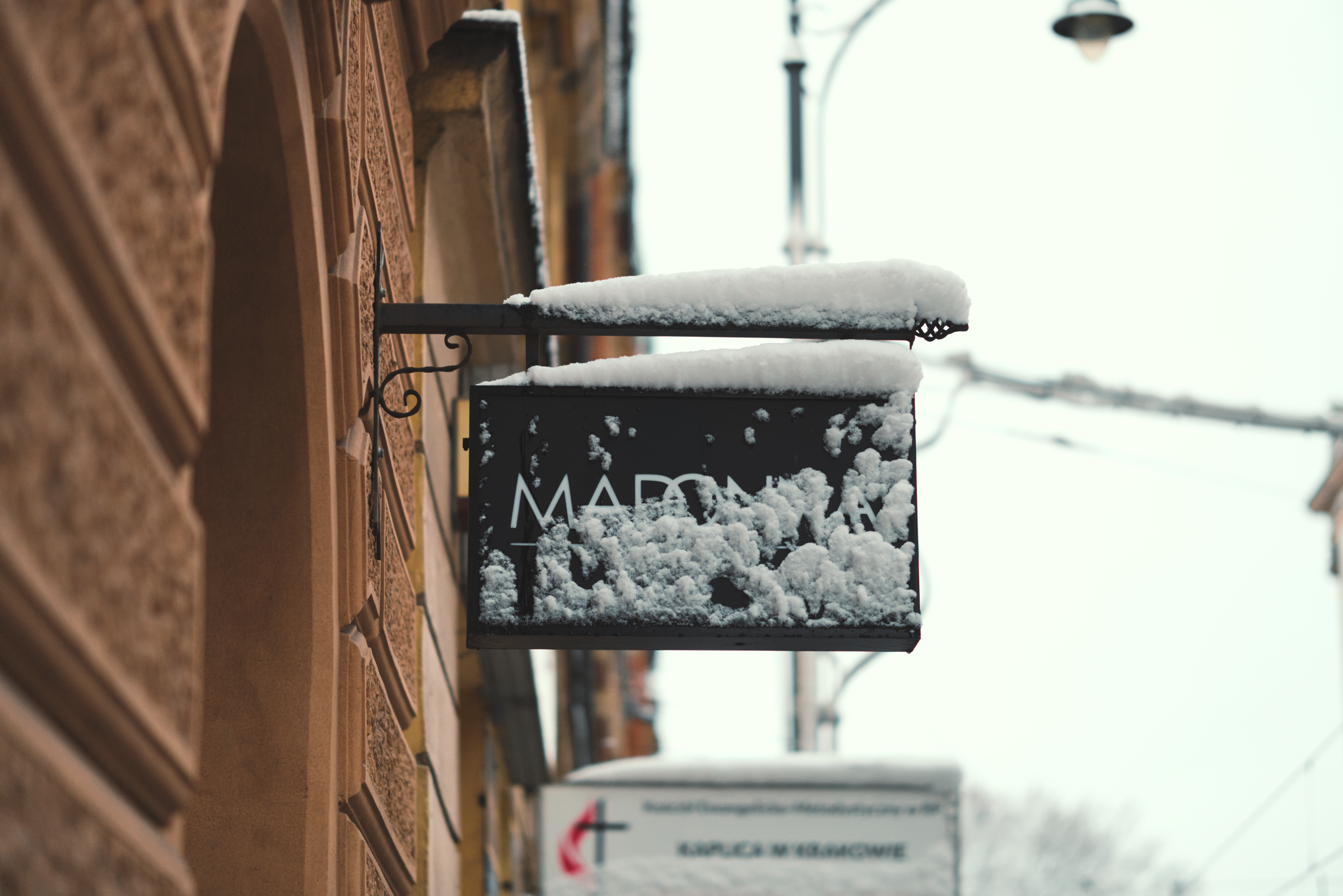 A snow-covered sign along a historic street in Krakow, Poland, during winter.