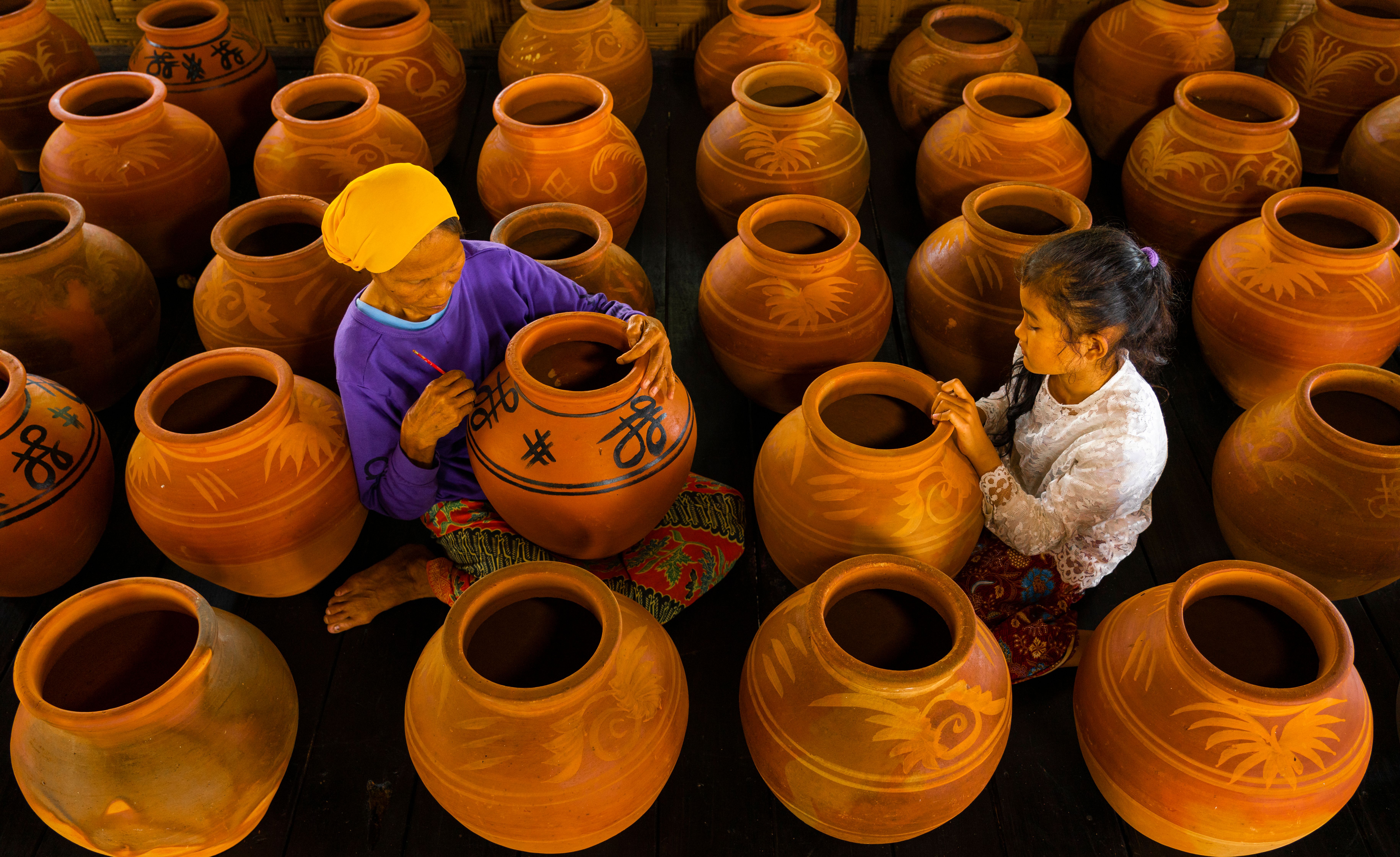 Two artisans engaged in decorating clay pots in a traditional setting, showcasing craftsmanship and culture.