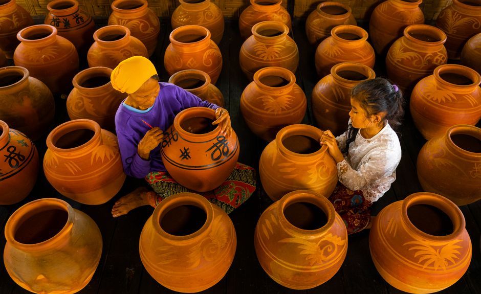 Two artisans engaged in decorating clay pots in a traditional setting, showcasing craftsmanship and culture.