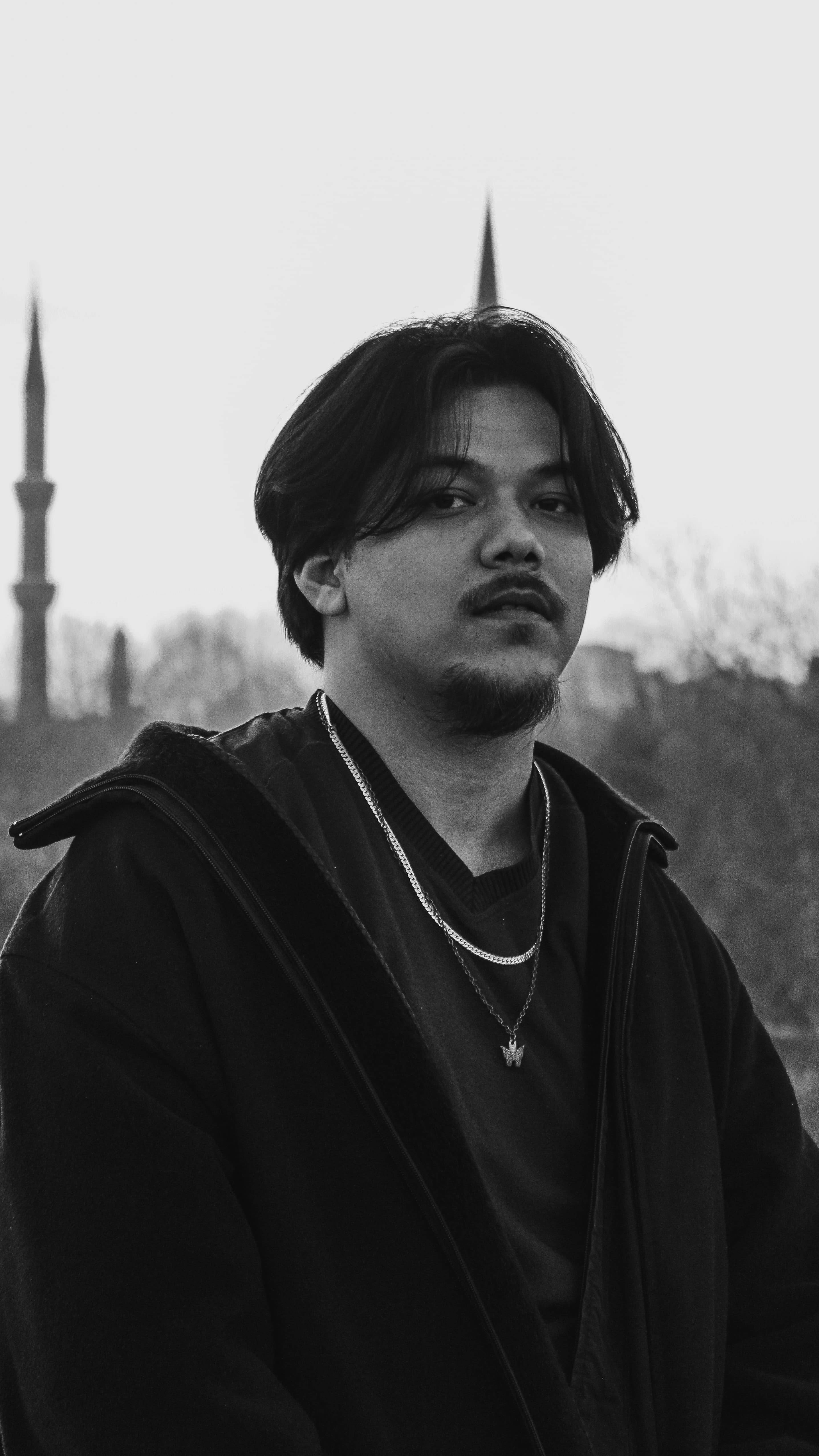 Black and white portrait of a man standing outdoors with blurred background.